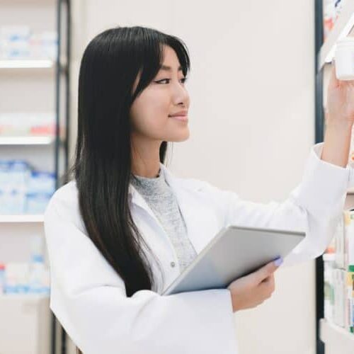 Druggist holding remedy pills, learning new medicines goods with tablet on shelves of pharmacy