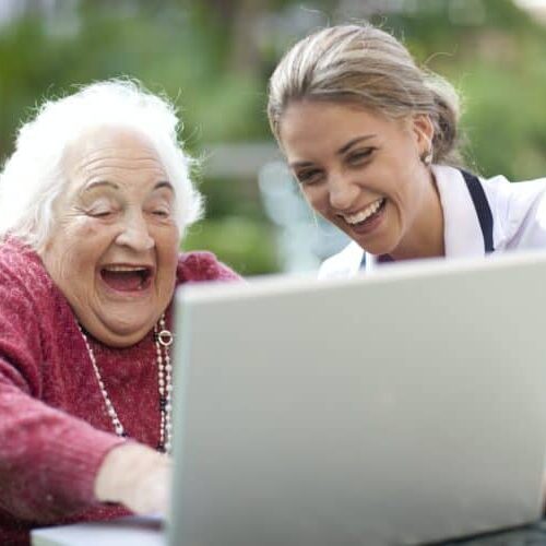 Happy nurse and senior woman using laptop together